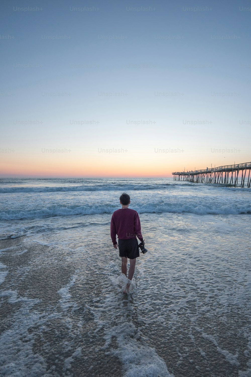 Una persona caminando hacia el océano al atardecer