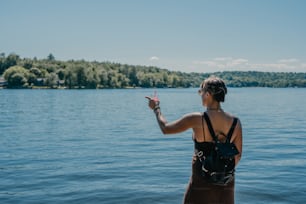 a woman is standing on the edge of a lake pointing at something