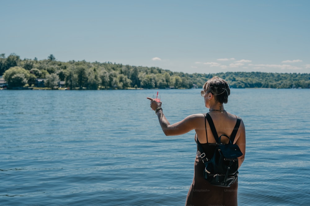 a woman is standing on the edge of a lake pointing at something