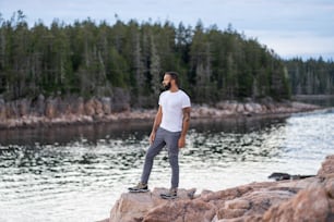 Un hombre parado en una roca cerca de un cuerpo de agua