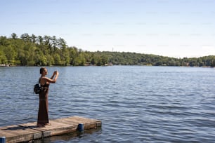 Eine Frau, die auf einem Dock steht und ein Foto vom Wasser macht