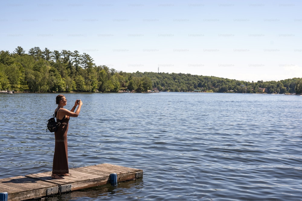 a woman standing on a dock taking a picture of the water