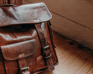 a brown leather backpack sitting on top of a wooden floor