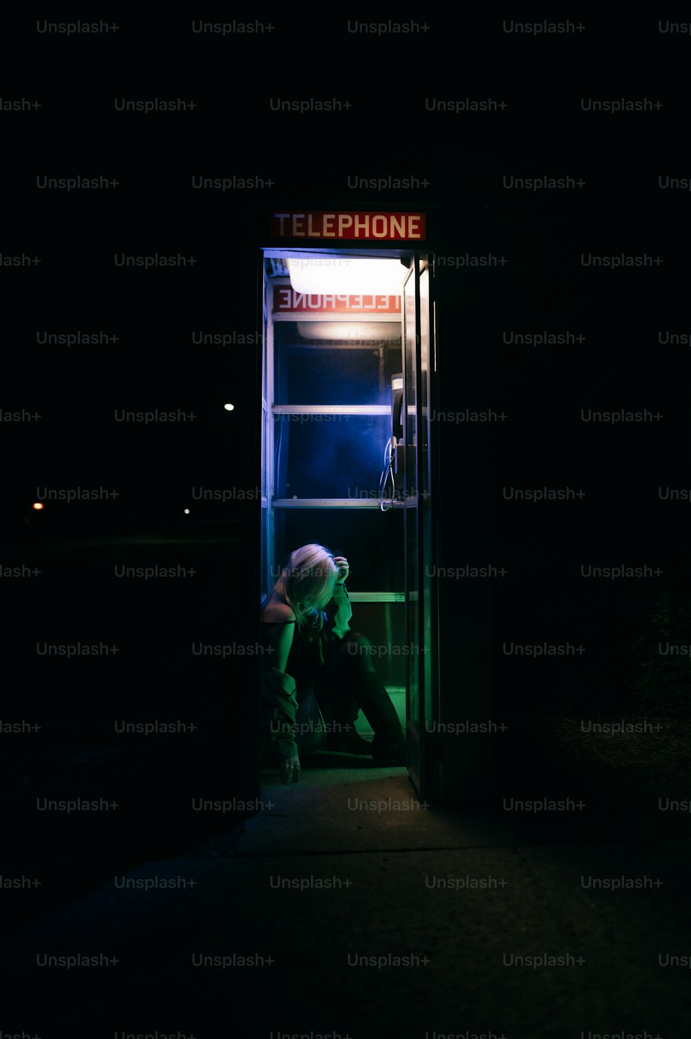 Una persona sentada en una cabina telefónica por la noche