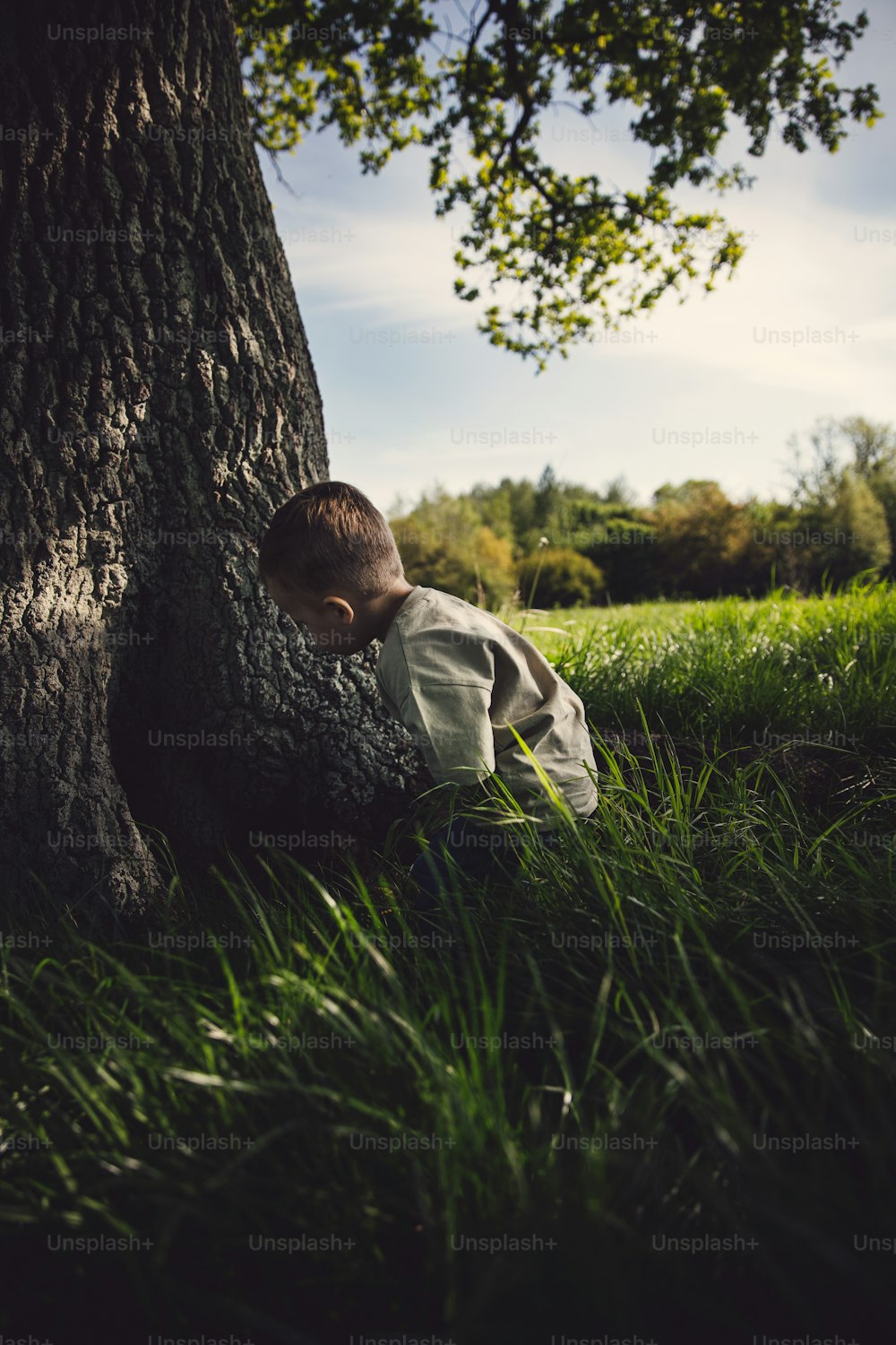 a young boy laying on the ground next to a tree