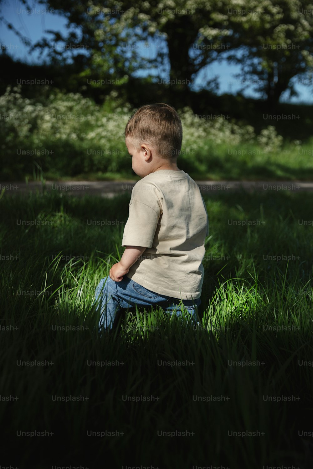 a little boy sitting in the grass looking at something