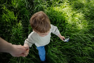 a little boy holding a cell phone in a field