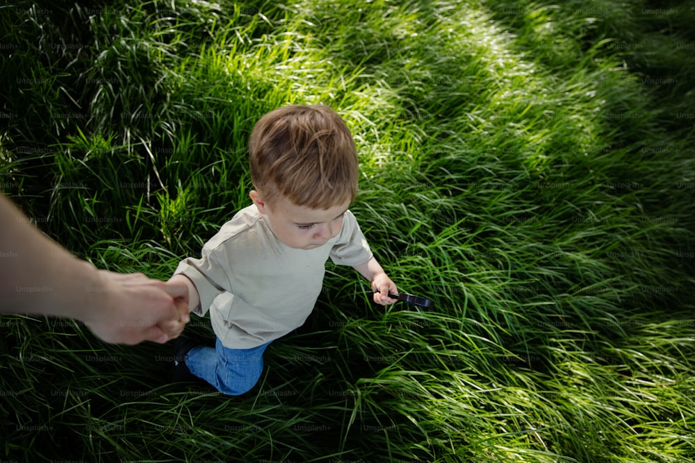 a little boy sitting in the grass holding a remote control