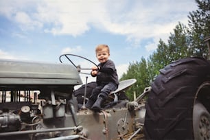a young boy sitting on the front of an old tractor