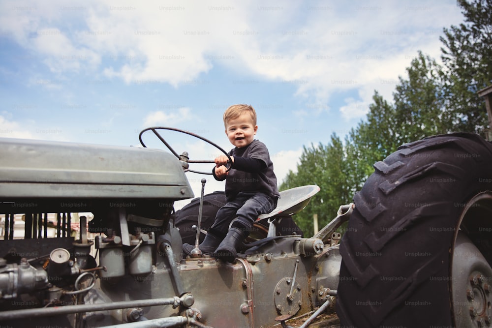 a young boy sitting on the front of an old tractor