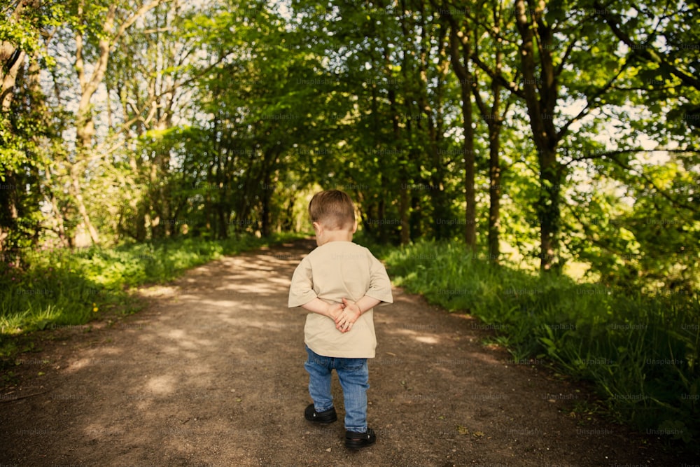 a little boy walking down a dirt road in the woods