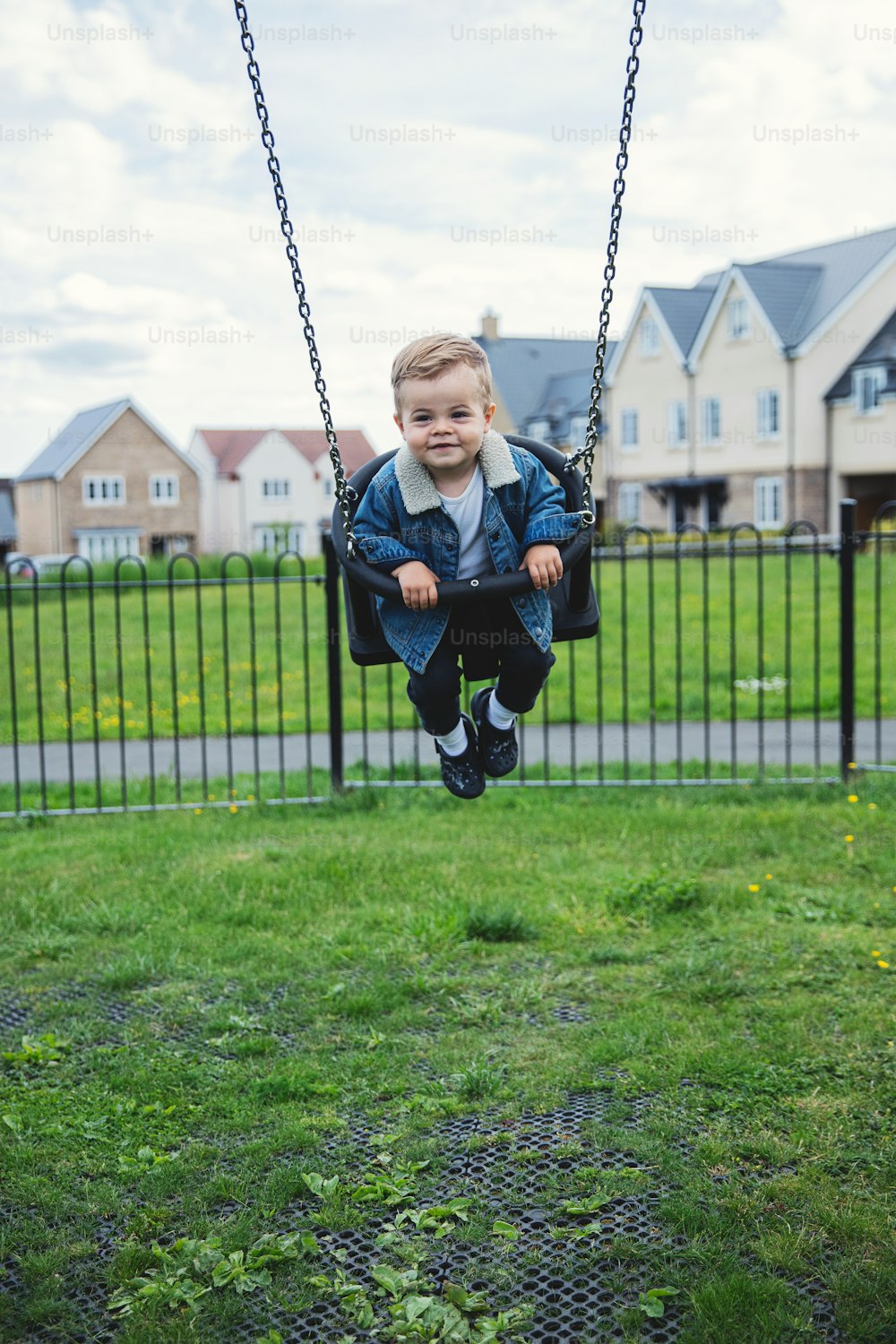 a little boy sitting on a swing in a park