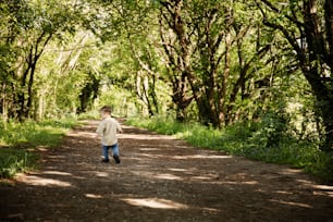 a young boy walking down a dirt road in the woods