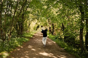 a man walking down a dirt road surrounded by trees