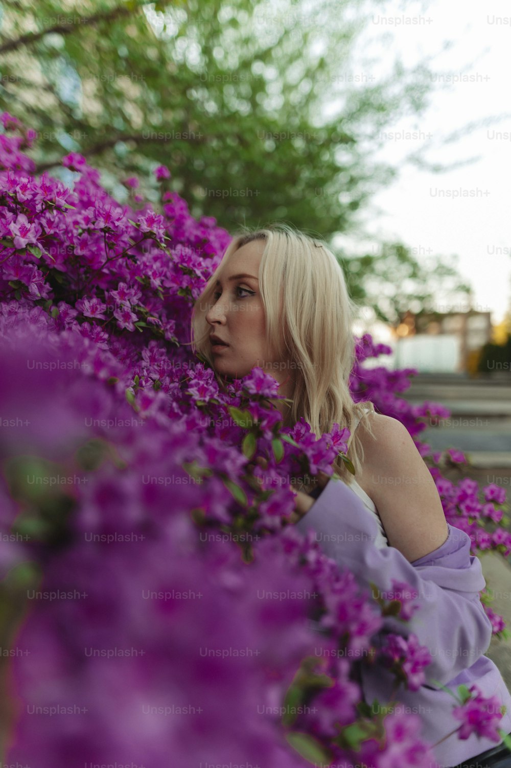 a woman in a purple top is leaning against a bush of purple flowers