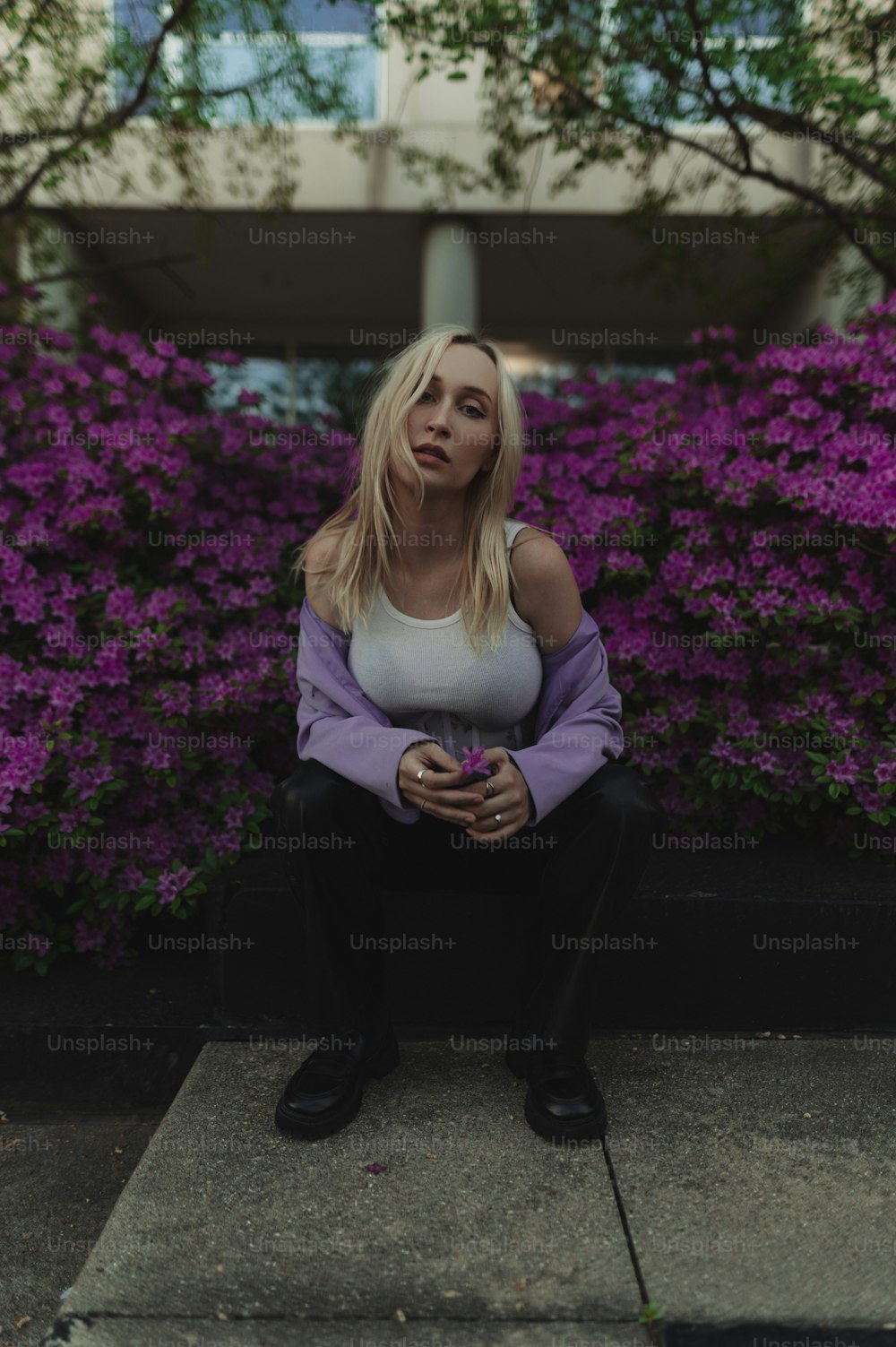 a woman sitting on a curb in front of purple flowers