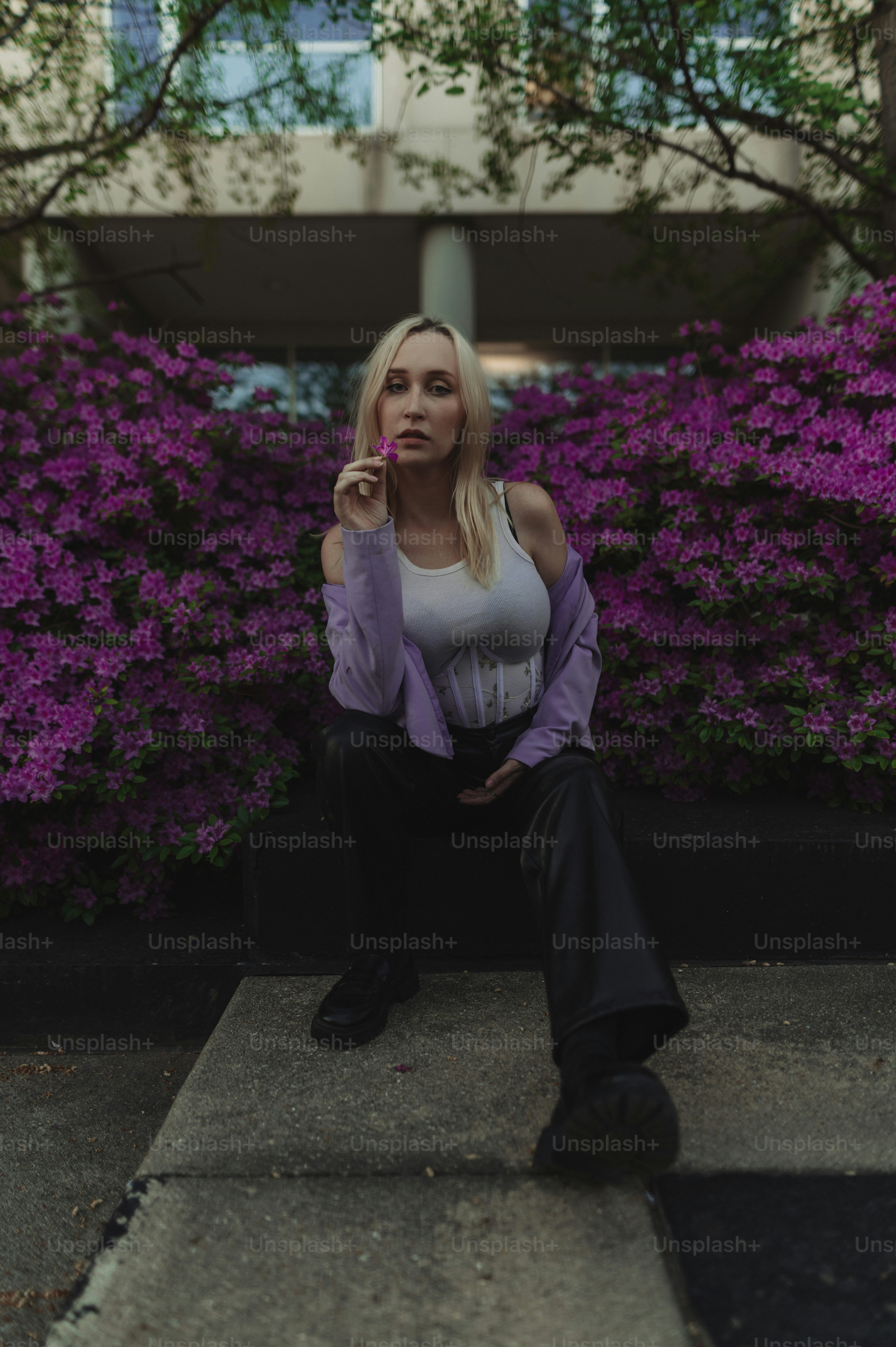 A woman sitting on a step in front of purple flowers photo – Blonde ...