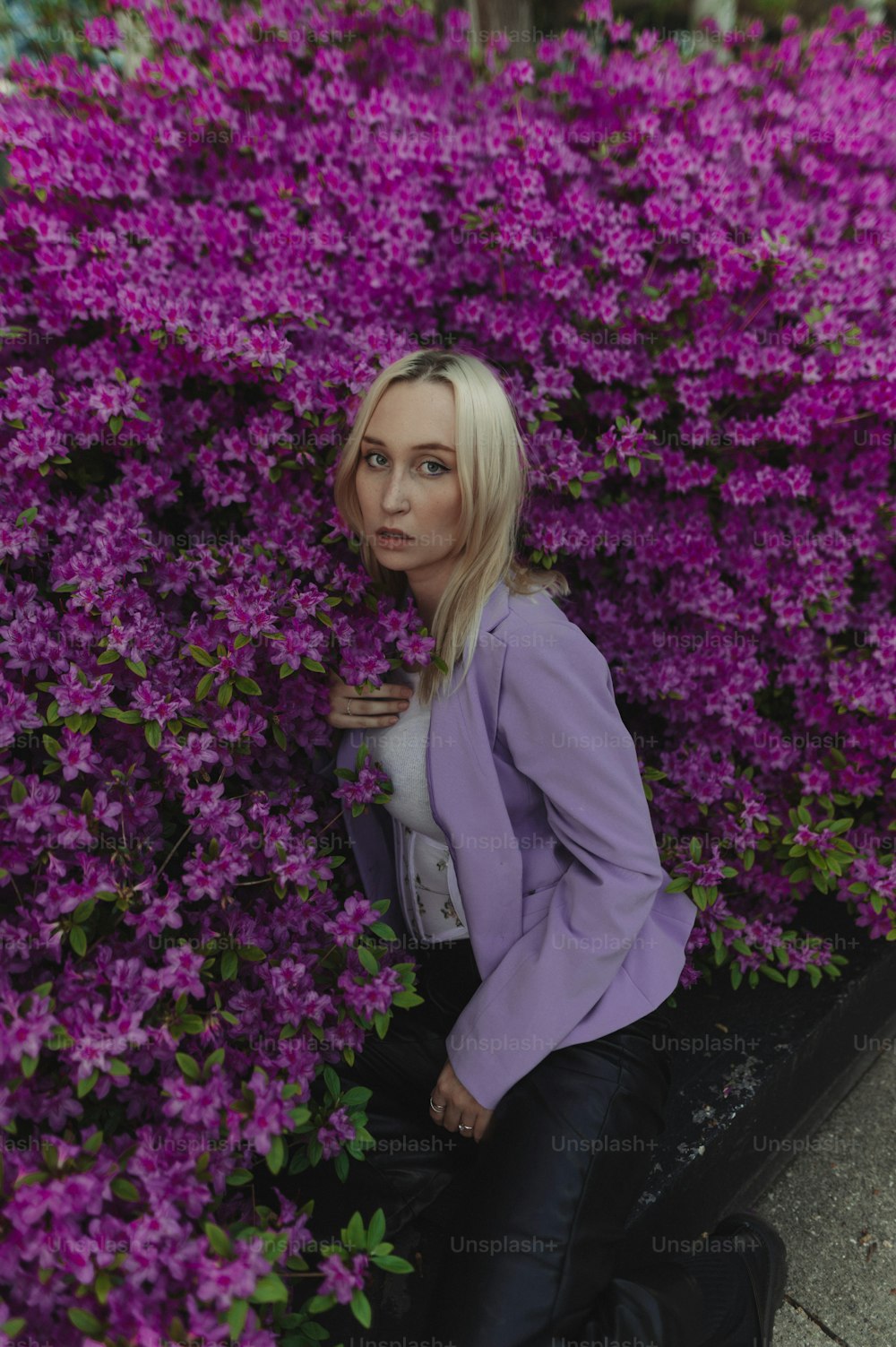 a woman sitting on a suitcase in front of purple flowers
