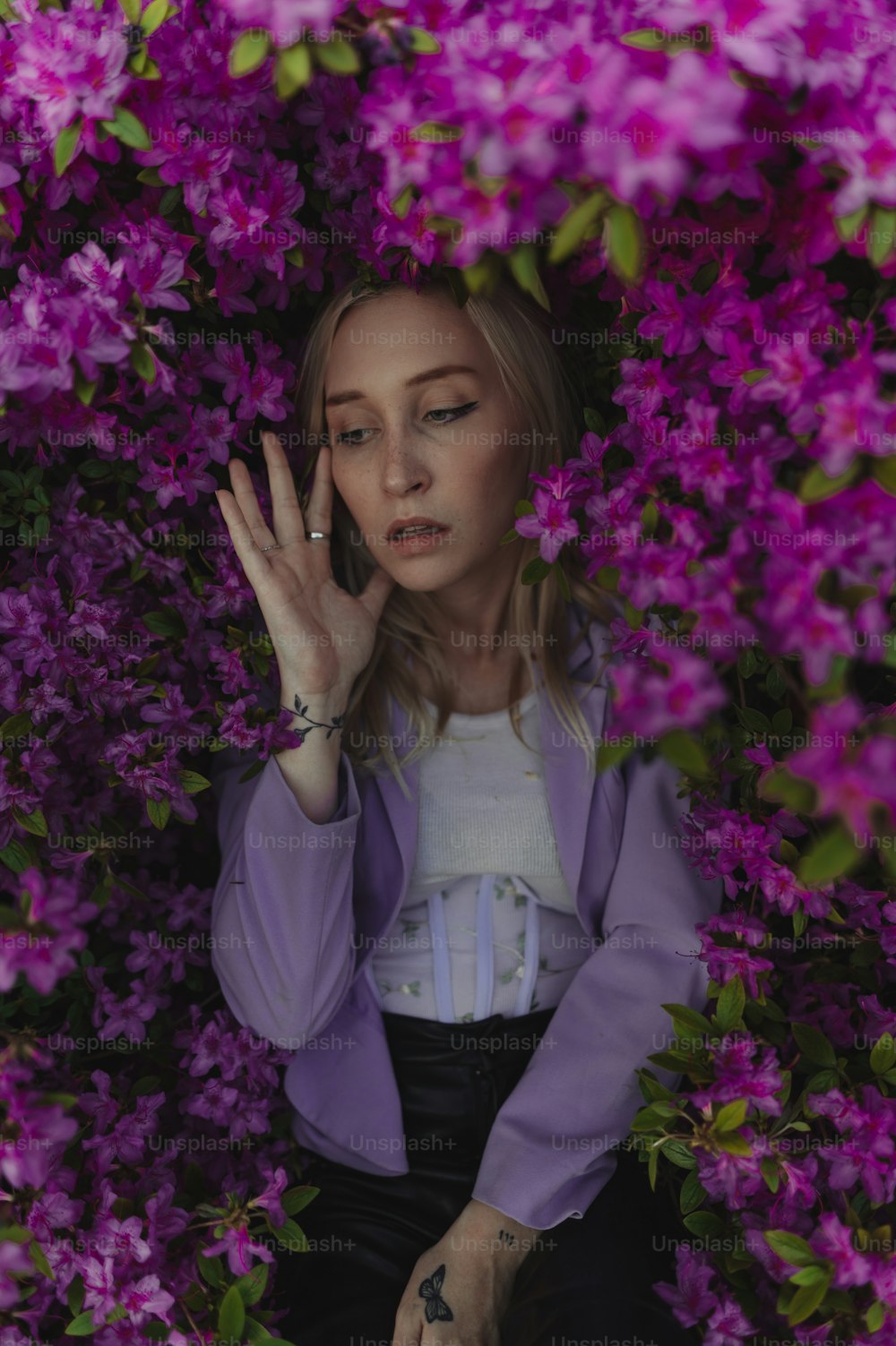 a woman sitting in a bush of flowers talking on a cell phone