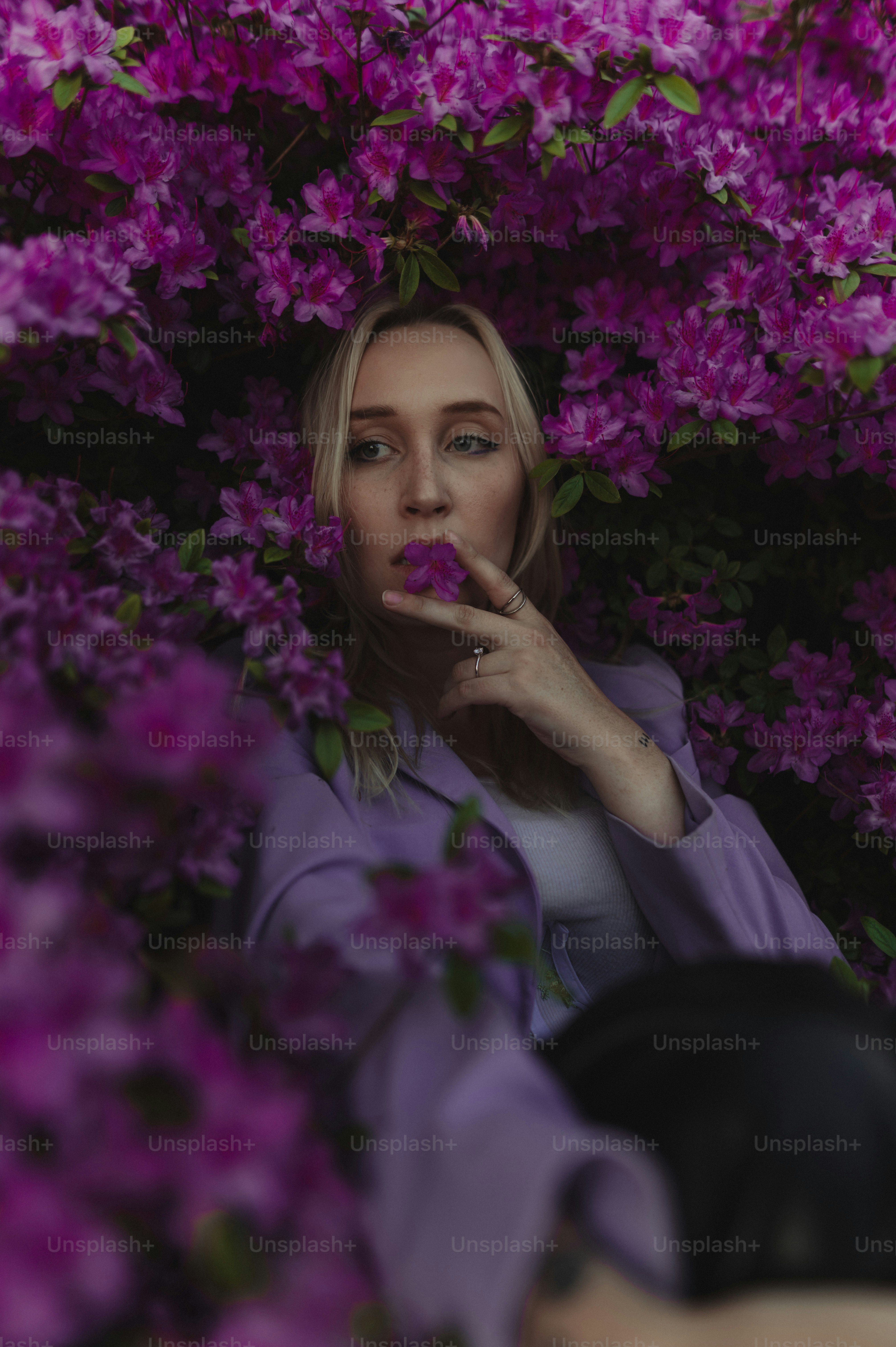 a woman standing in front of a bush of purple flowers