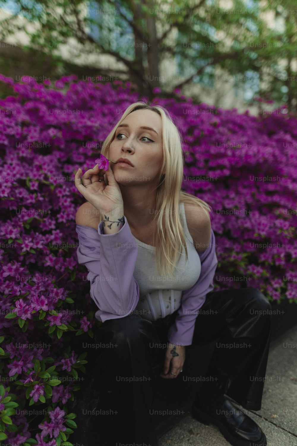a woman sitting on the ground next to purple flowers