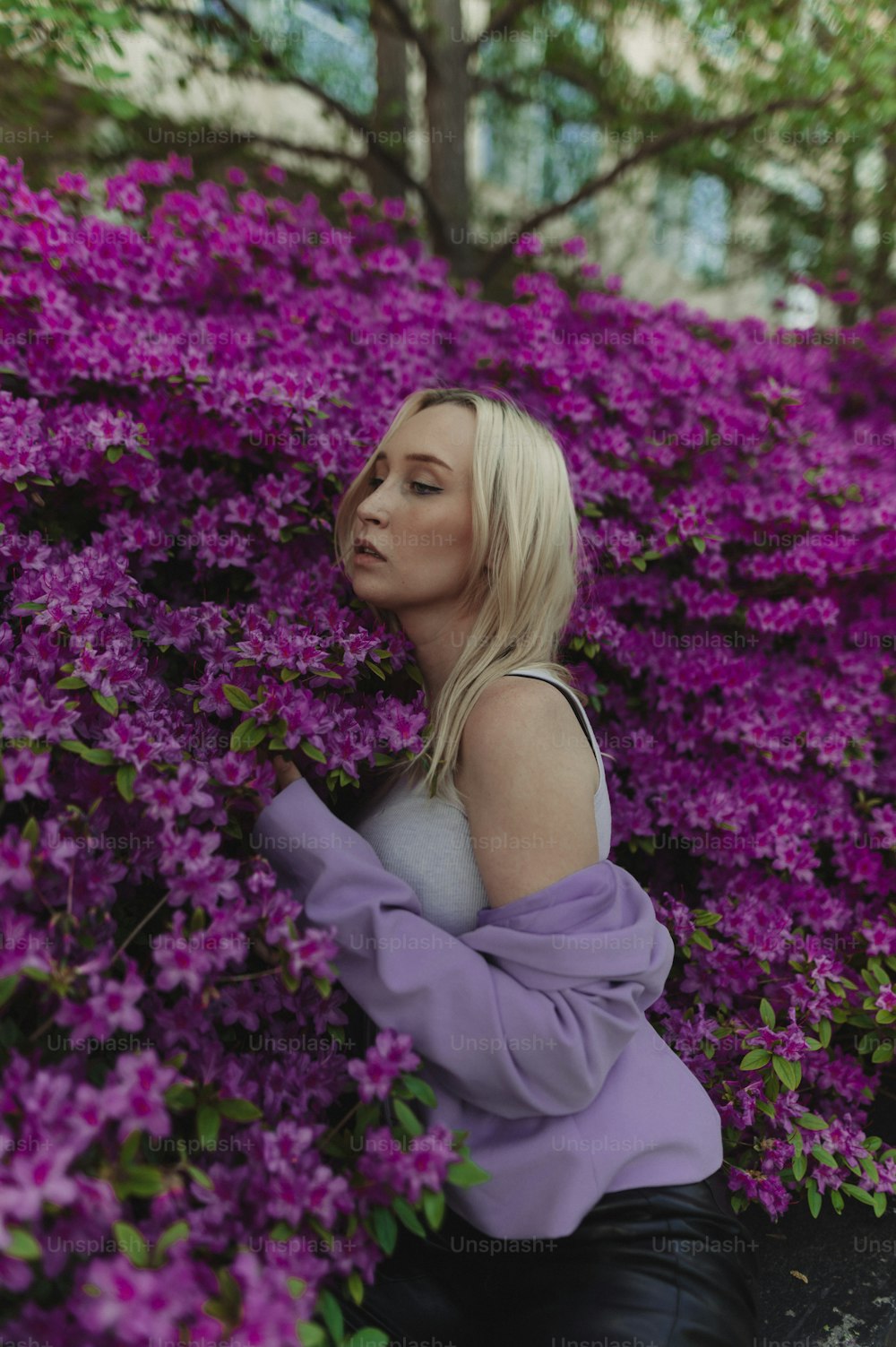 a woman sitting in front of a bush of purple flowers