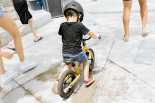 a little boy riding a yellow bike down a sidewalk
