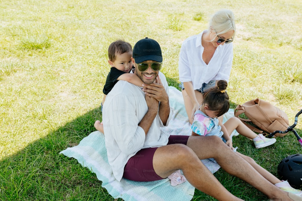 Une femme et deux enfants assis sur une couverture dans l’herbe
