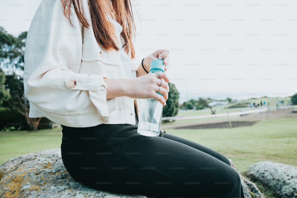a woman sitting on a rock holding a water bottle