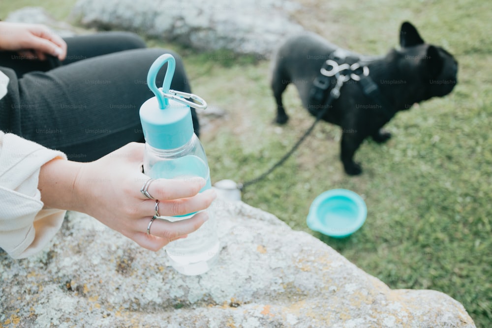 a woman holding a water bottle next to a black dog