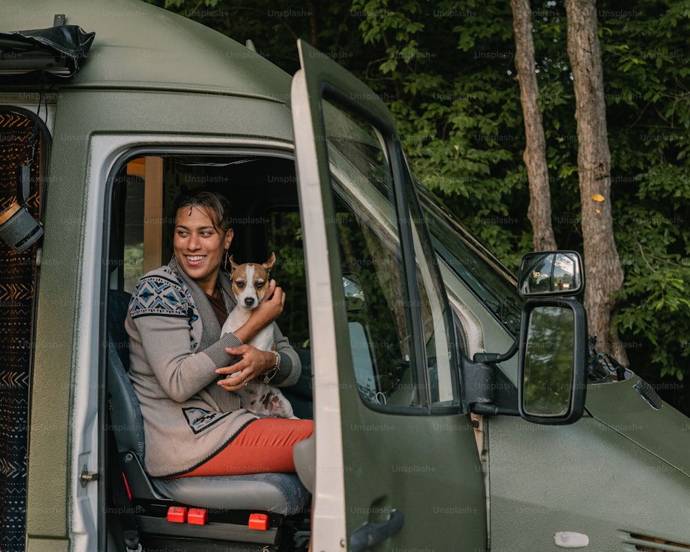 a woman sitting in the driver's seat of a truck holding a dog
