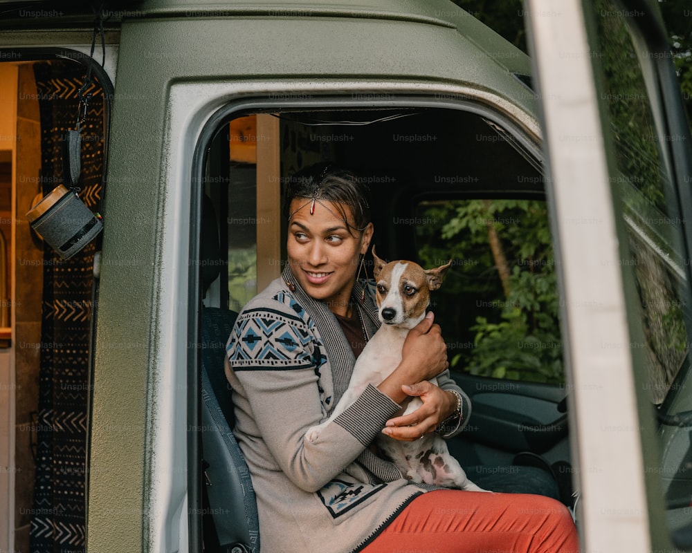 Un homme tenant un petit chien assis sur le siège du conducteur d’un camion