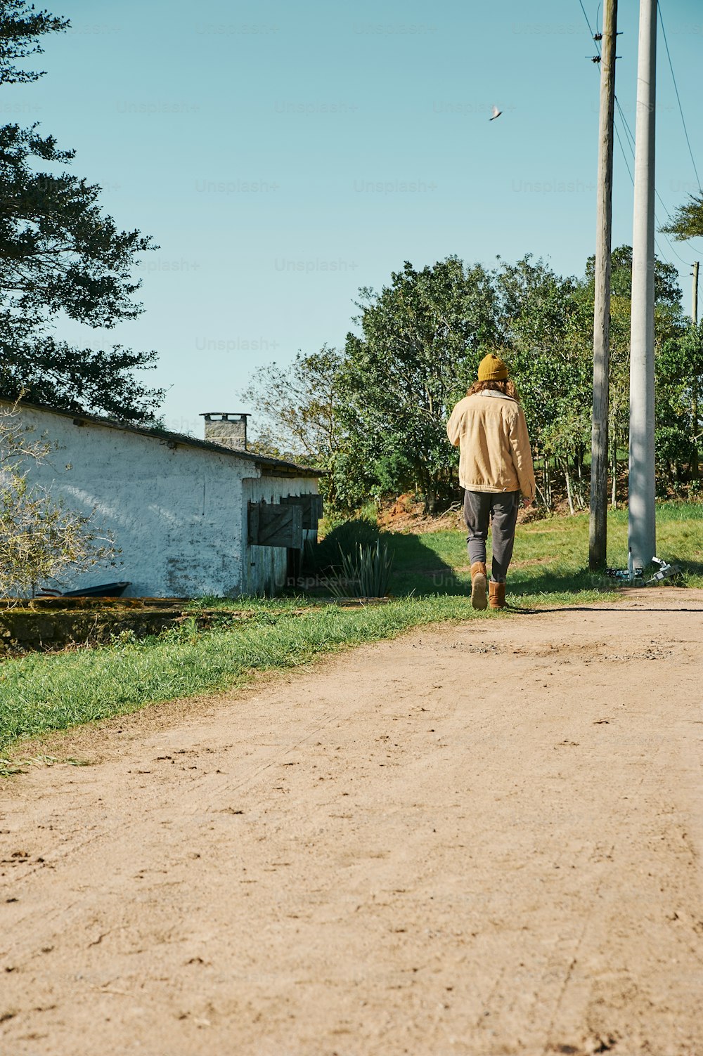 a man walking down a dirt road next to a house