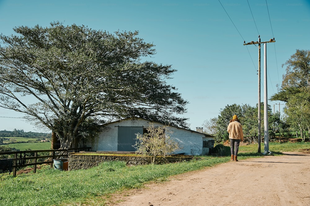 a man walking down a dirt road next to a tree