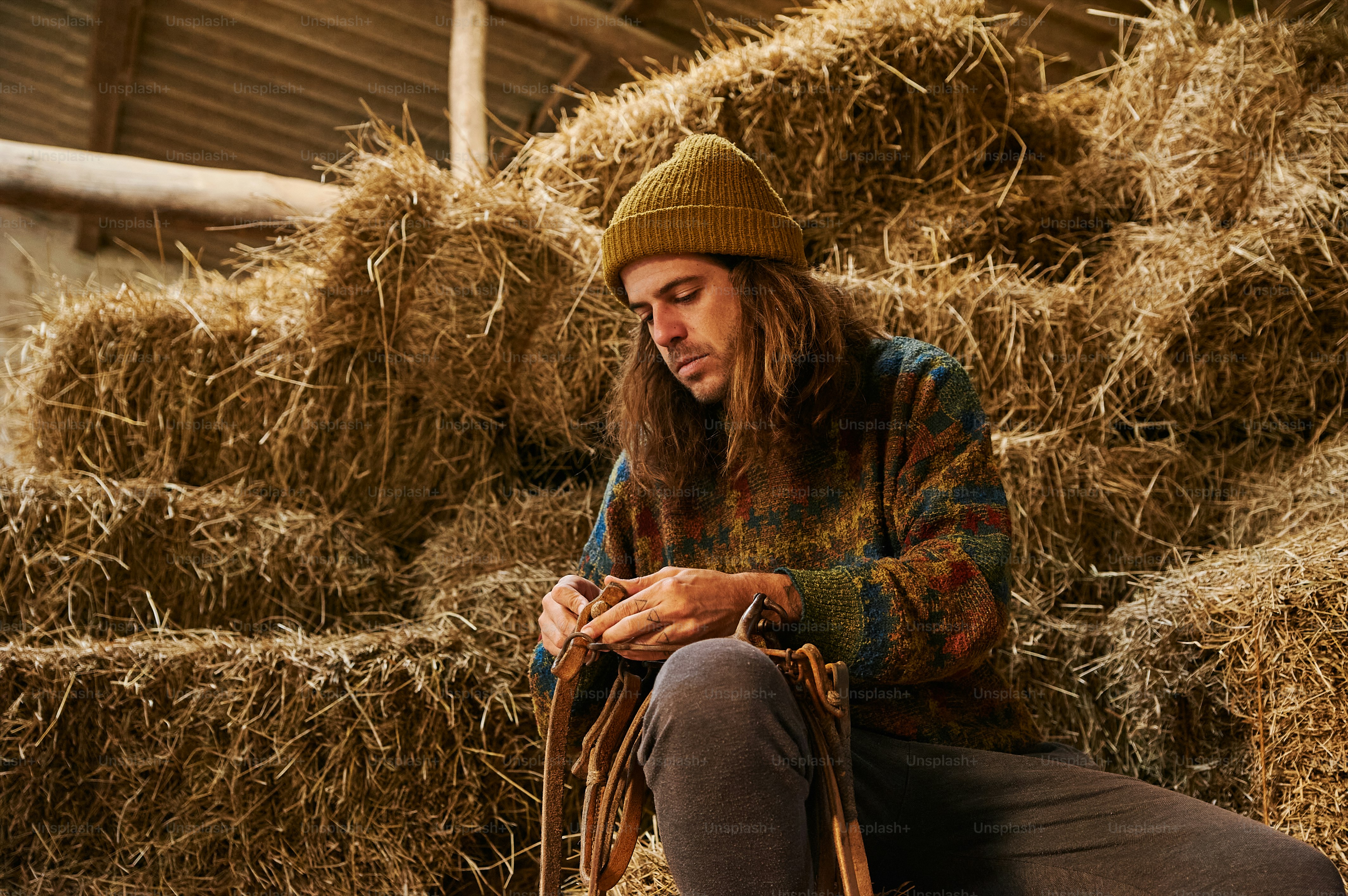 a man sitting on a pile of hay looking at his cell phone