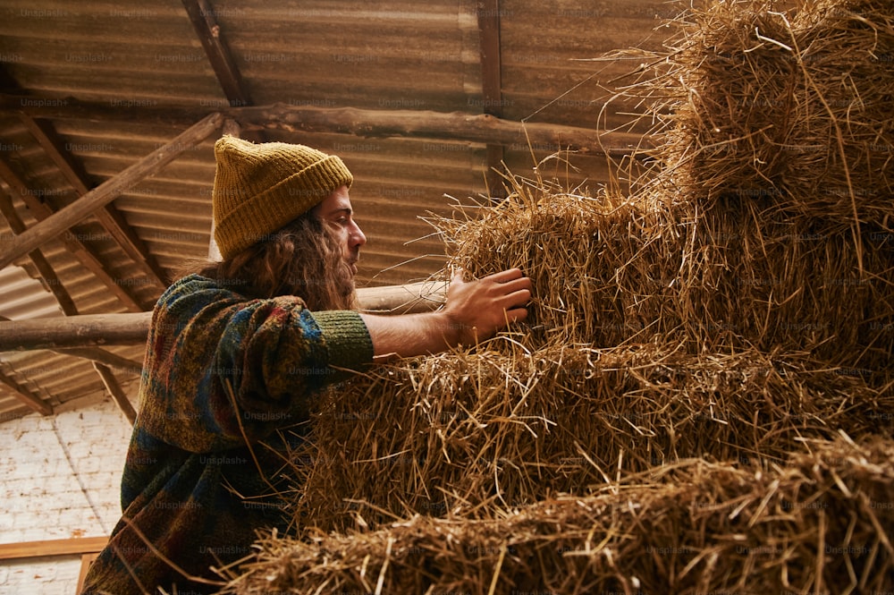 a man with long hair and a beard is holding a bale of hay