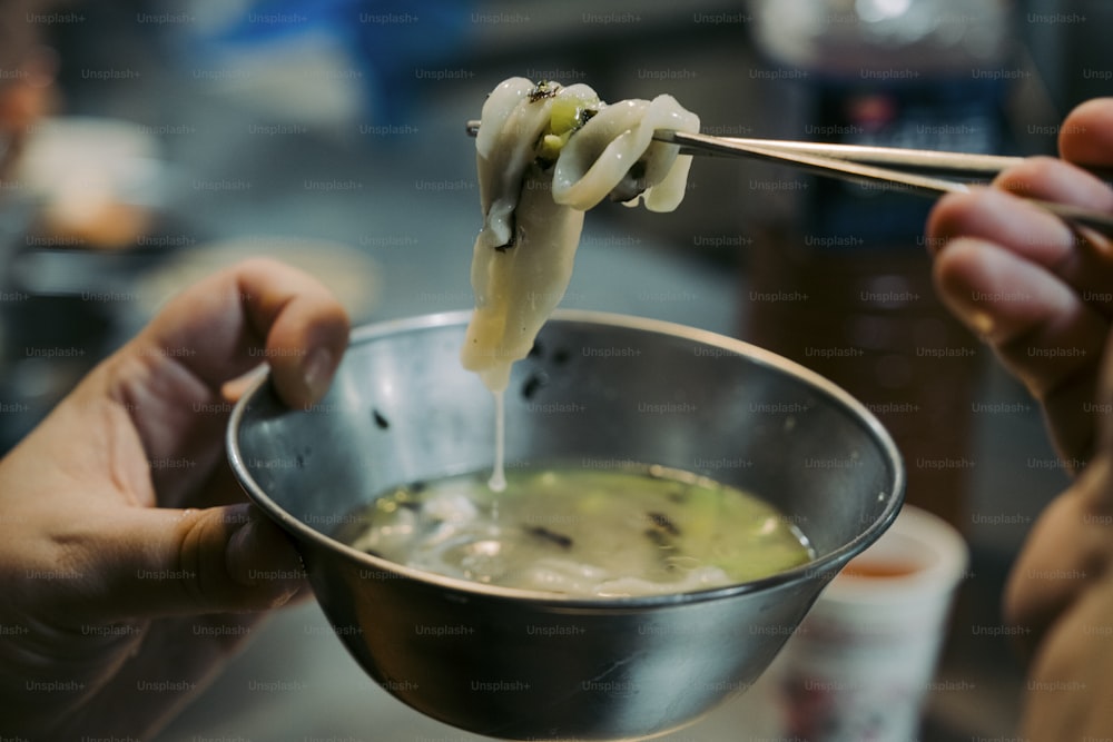 a person holding chopsticks over a bowl of soup