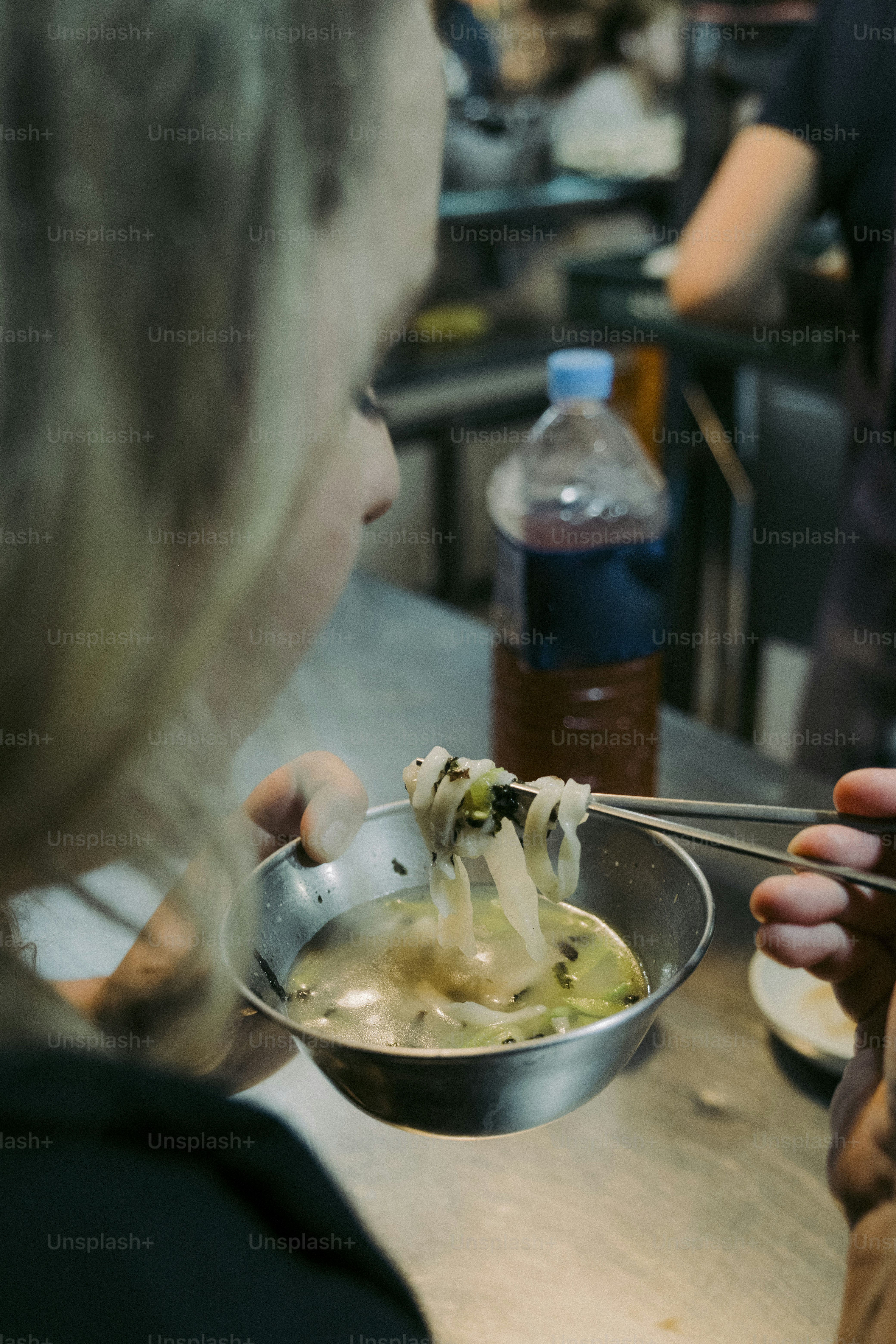 a woman eating a bowl of soup with chopsticks