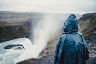 uma pessoa em uma capa de chuva olhando para uma cachoeira