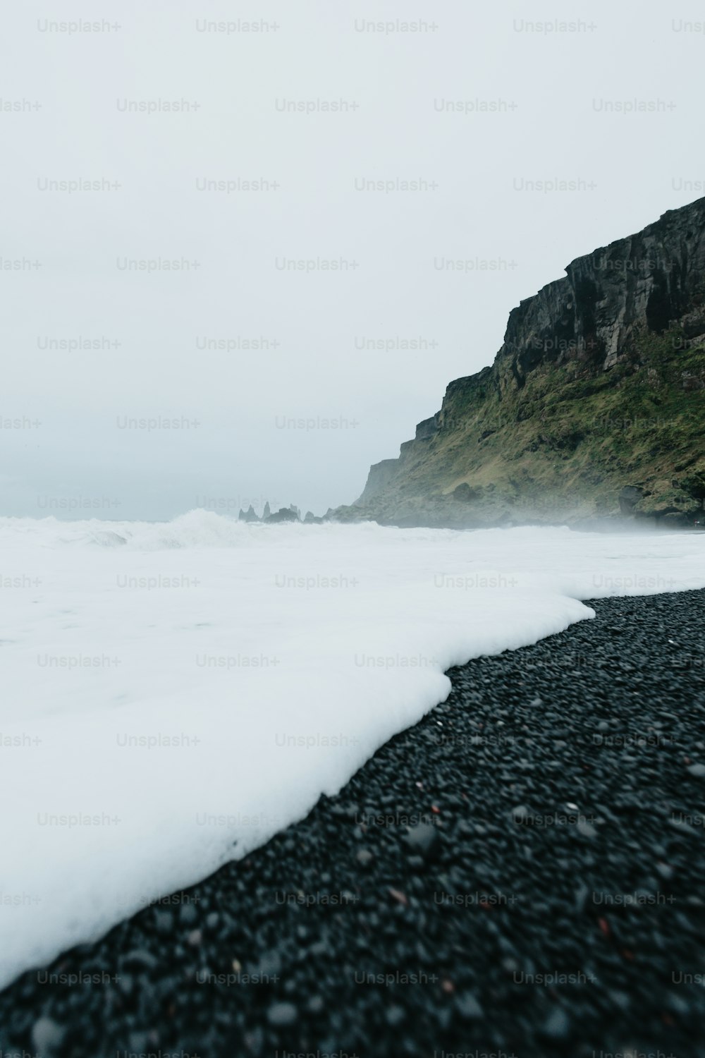 uma praia preta com um penhasco ao fundo