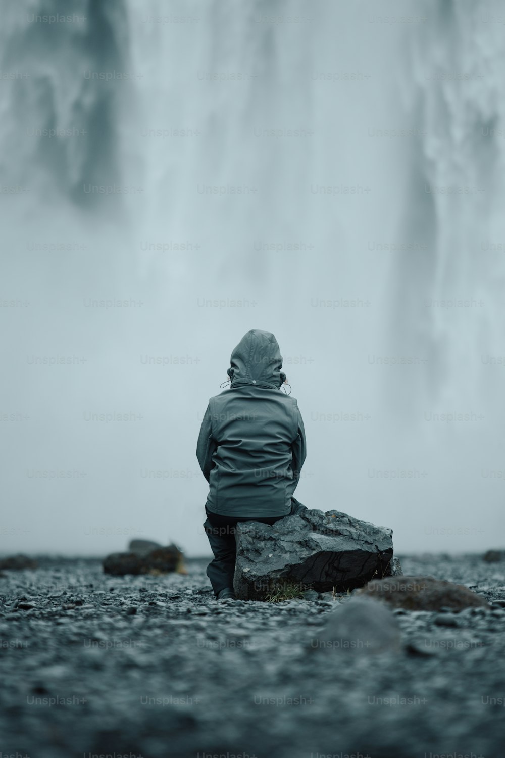 a person sitting on a rock in front of a waterfall