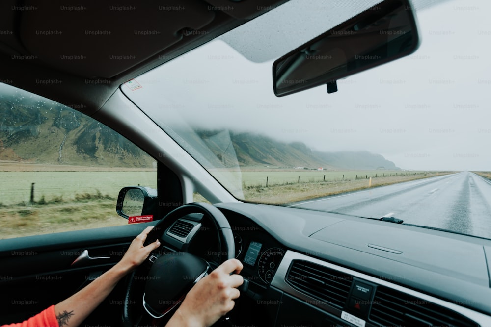 a person driving a car on a road with mountains in the background