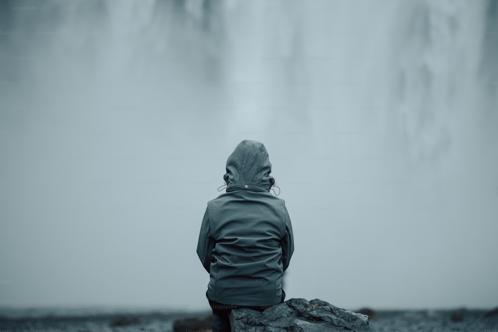 eine Person, die auf einem Felsen vor einem Wasserfall sitzt
