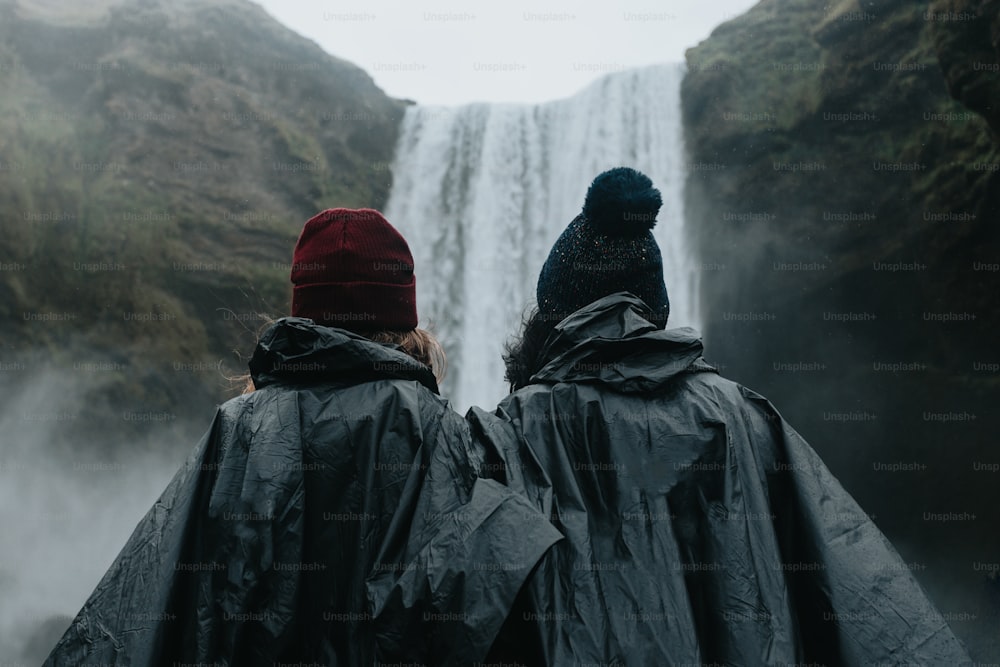 two people standing in front of a waterfall