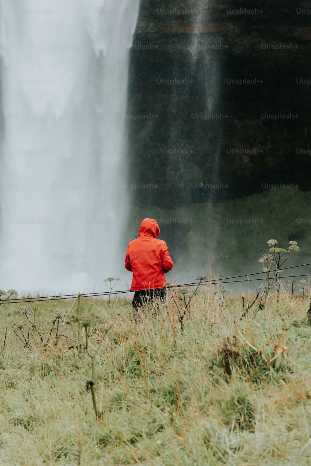 a person in a red jacket standing in front of a waterfall