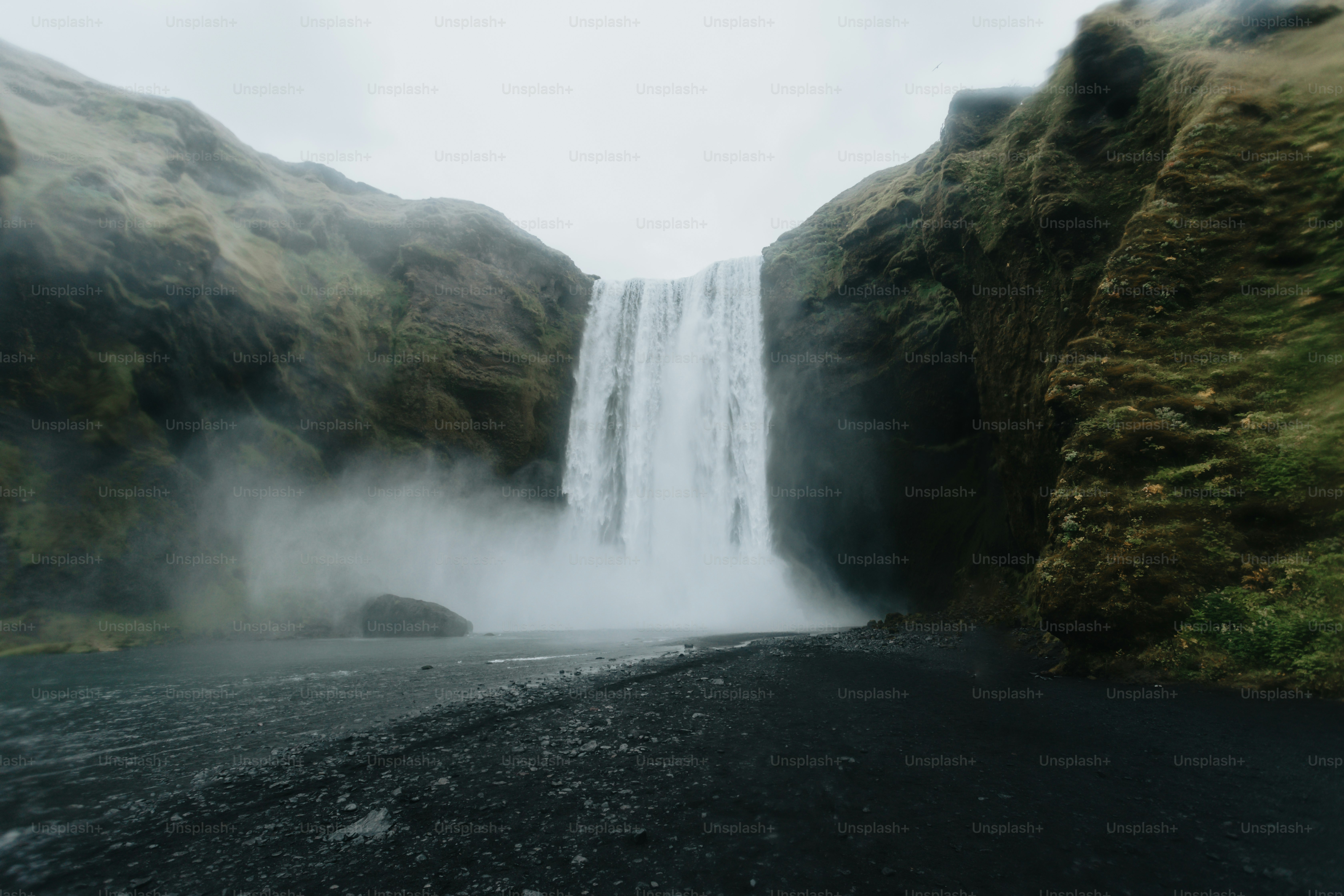 a very tall waterfall towering over a lush green hillside