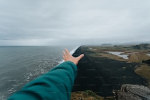 a person reaching out to the ocean from a cliff