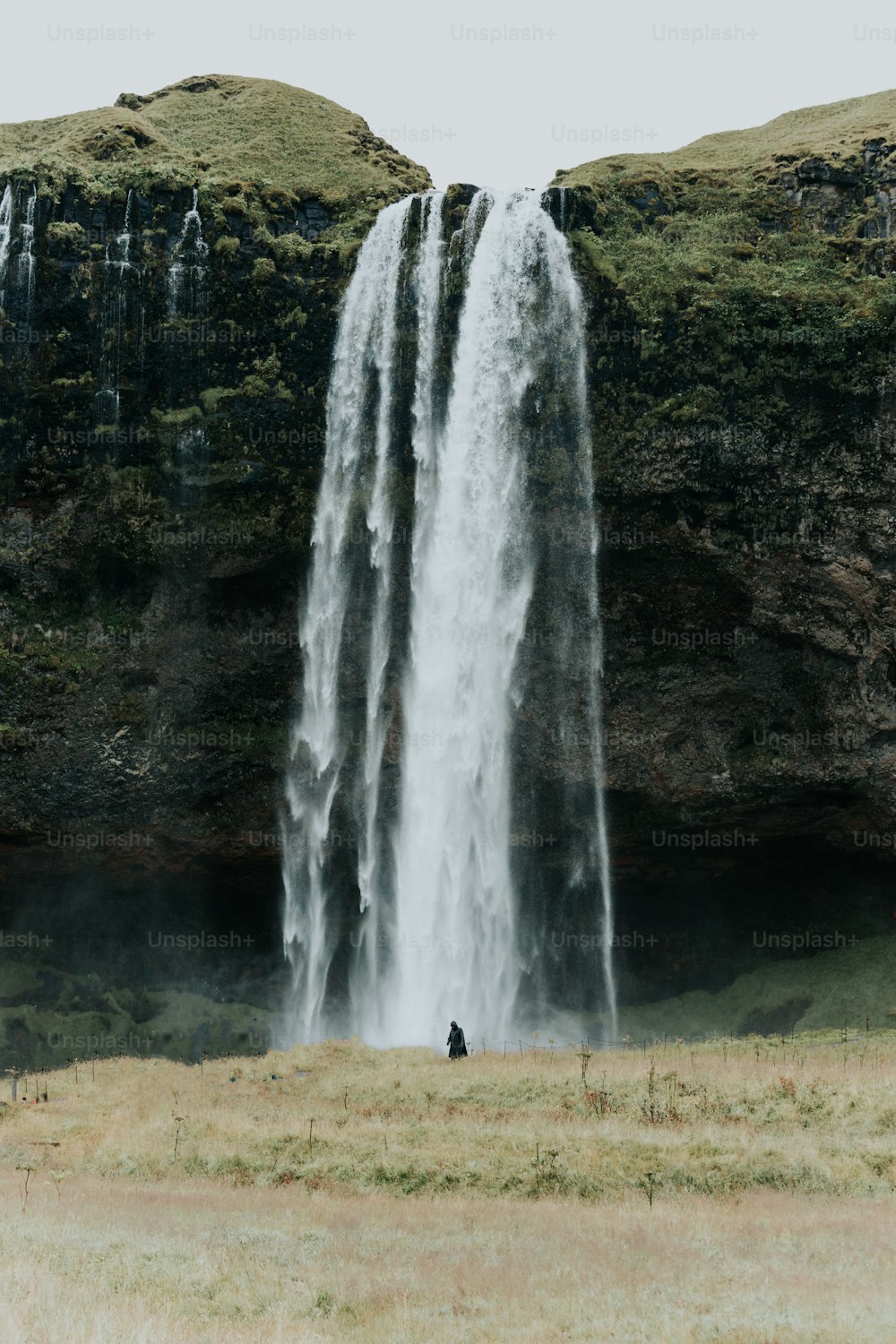a man standing in front of a tall waterfall