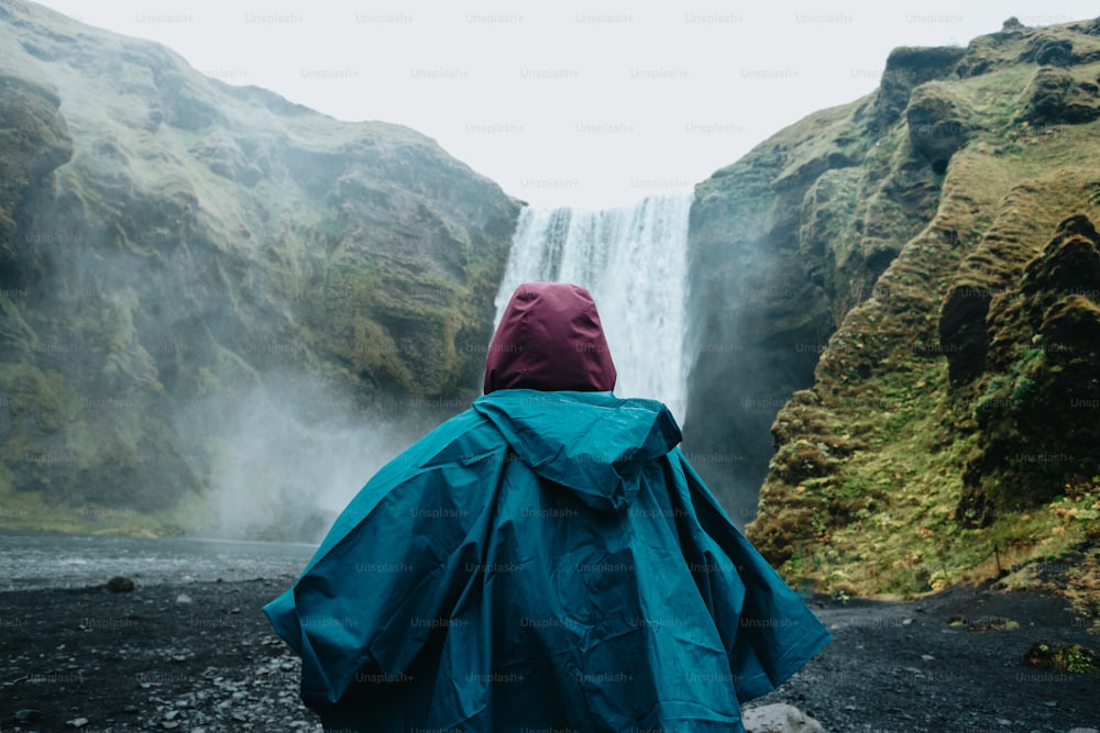 uma pessoa de capa de chuva em frente a uma cachoeira