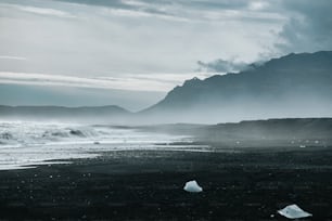 une photo en noir et blanc d’une plage avec des montagnes en arrière-plan